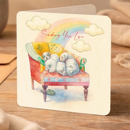 Watercolour greeting card featuring three sleeping puppies cuddled on a cozy armchair beneath a rainbow with the words ‘Sending You Love’.