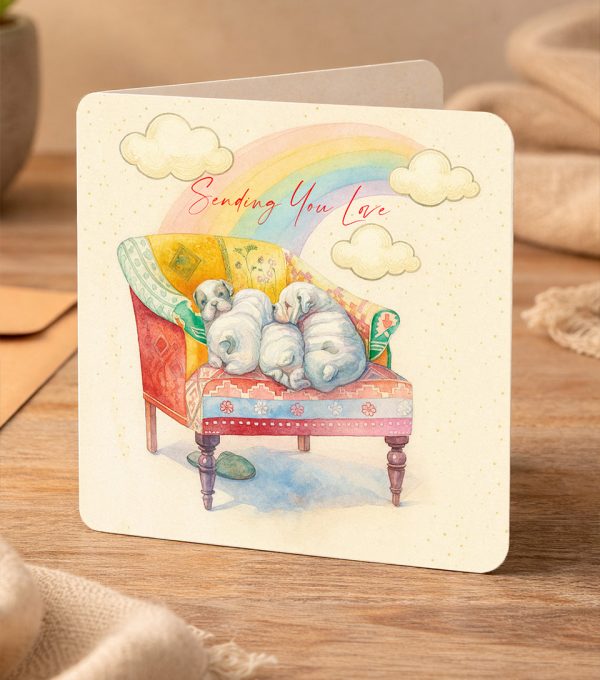 Watercolour greeting card featuring three sleeping puppies cuddled on a cozy armchair beneath a rainbow with the words ‘Sending You Love’.
